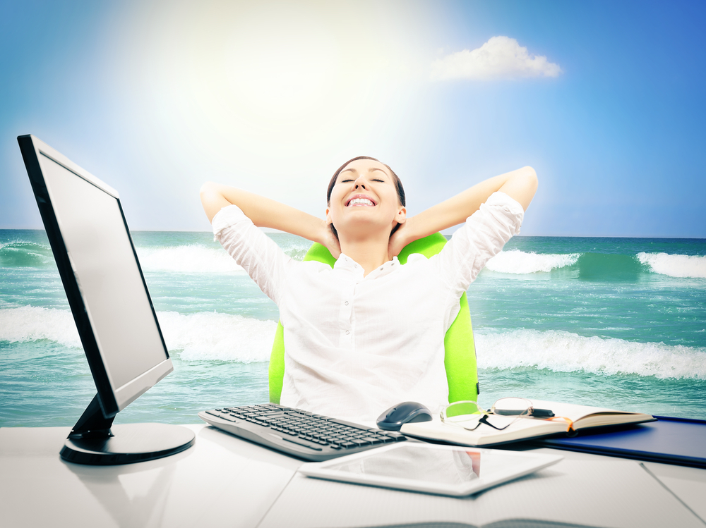 A woman sitting at her desk dreaming about vacation with an ocean background.